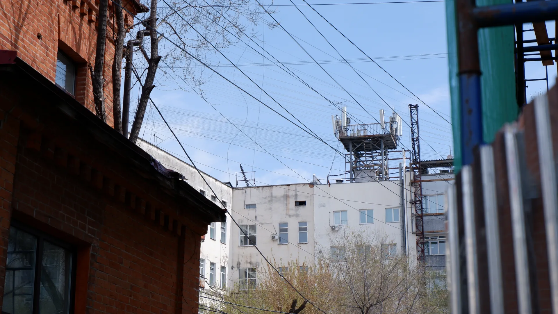 一栋红砖建筑旁边是一栋白色建筑,屋顶有通信塔。空中有许多电线,前景有金属栏杆。