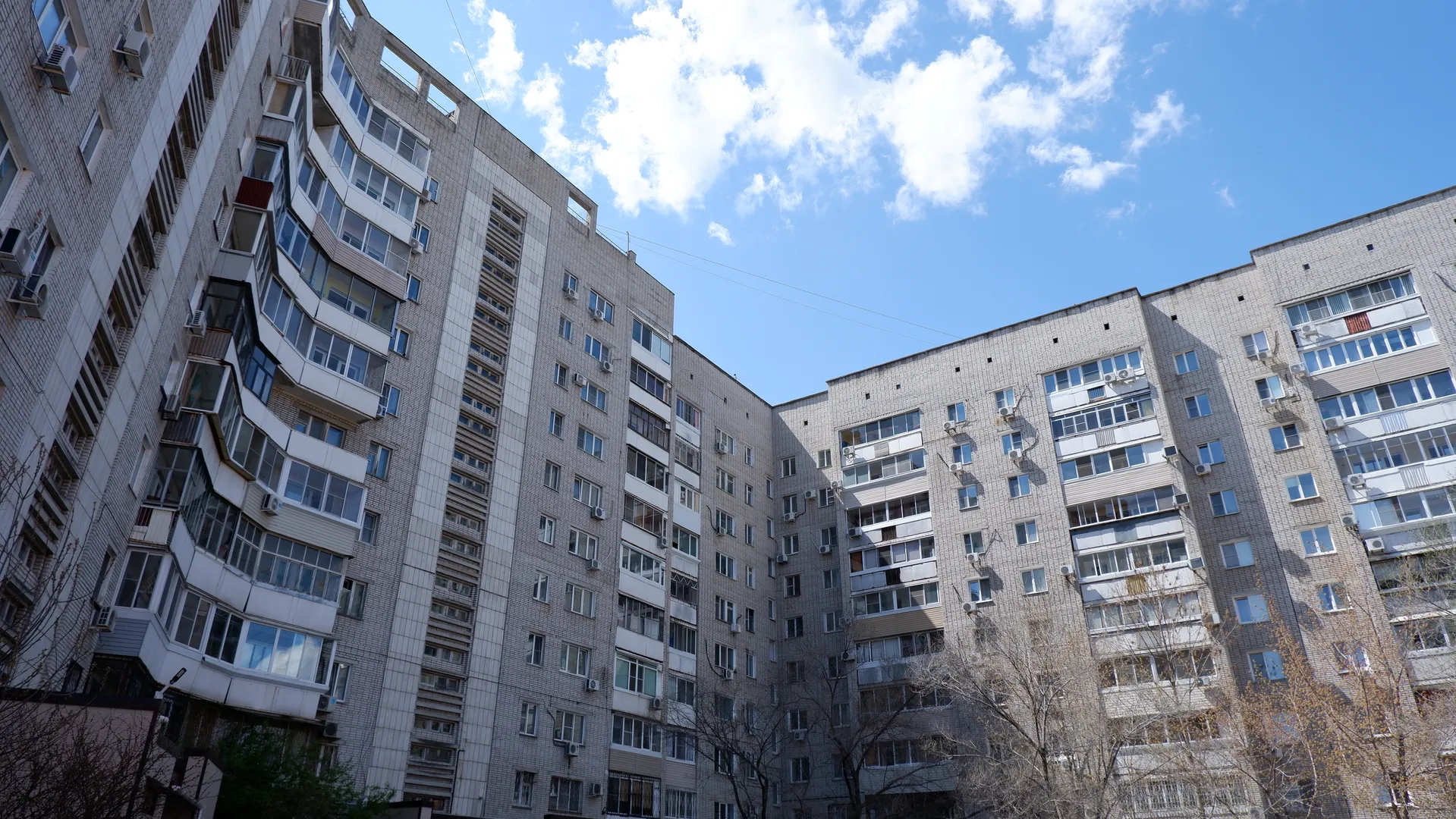 两栋高层建筑形成一个U形结构,外墙为灰色瓷砖,有许多窗户。建筑之间有一些树木,树叶稀疏。天空中有几朵白云。