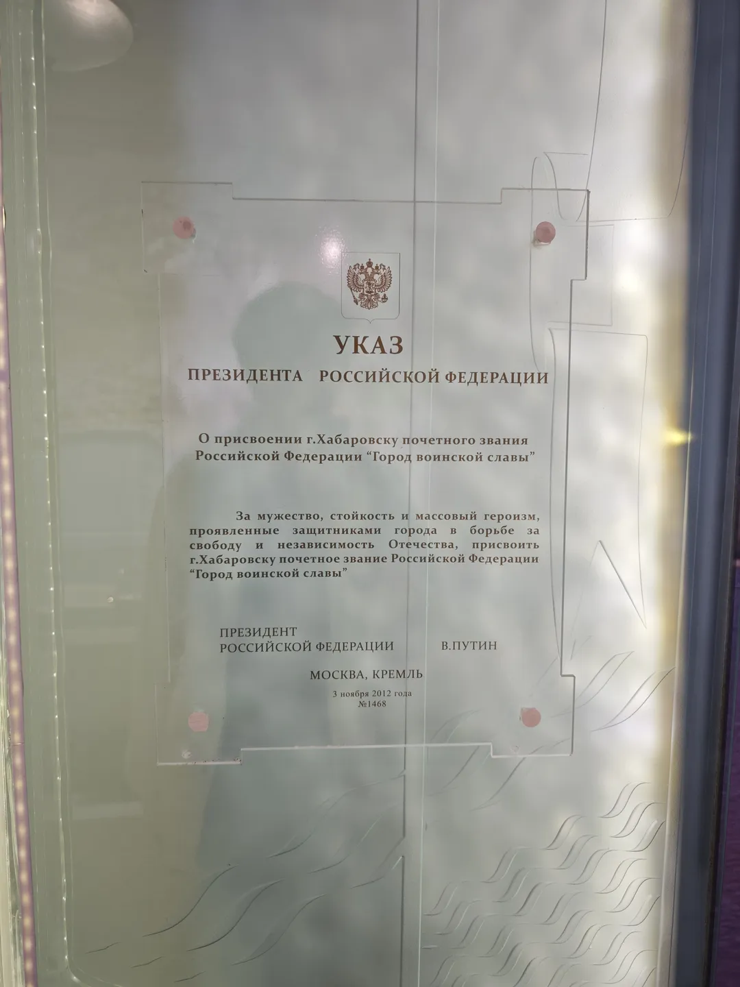一份文件被展示在一个透明玻璃柜中,文件顶部有国徽图案和“УКАЗ”字样。文件内容提到授予哈巴罗夫斯克市“军事荣耀之城”的称号。文件下方有总统签名和日期。