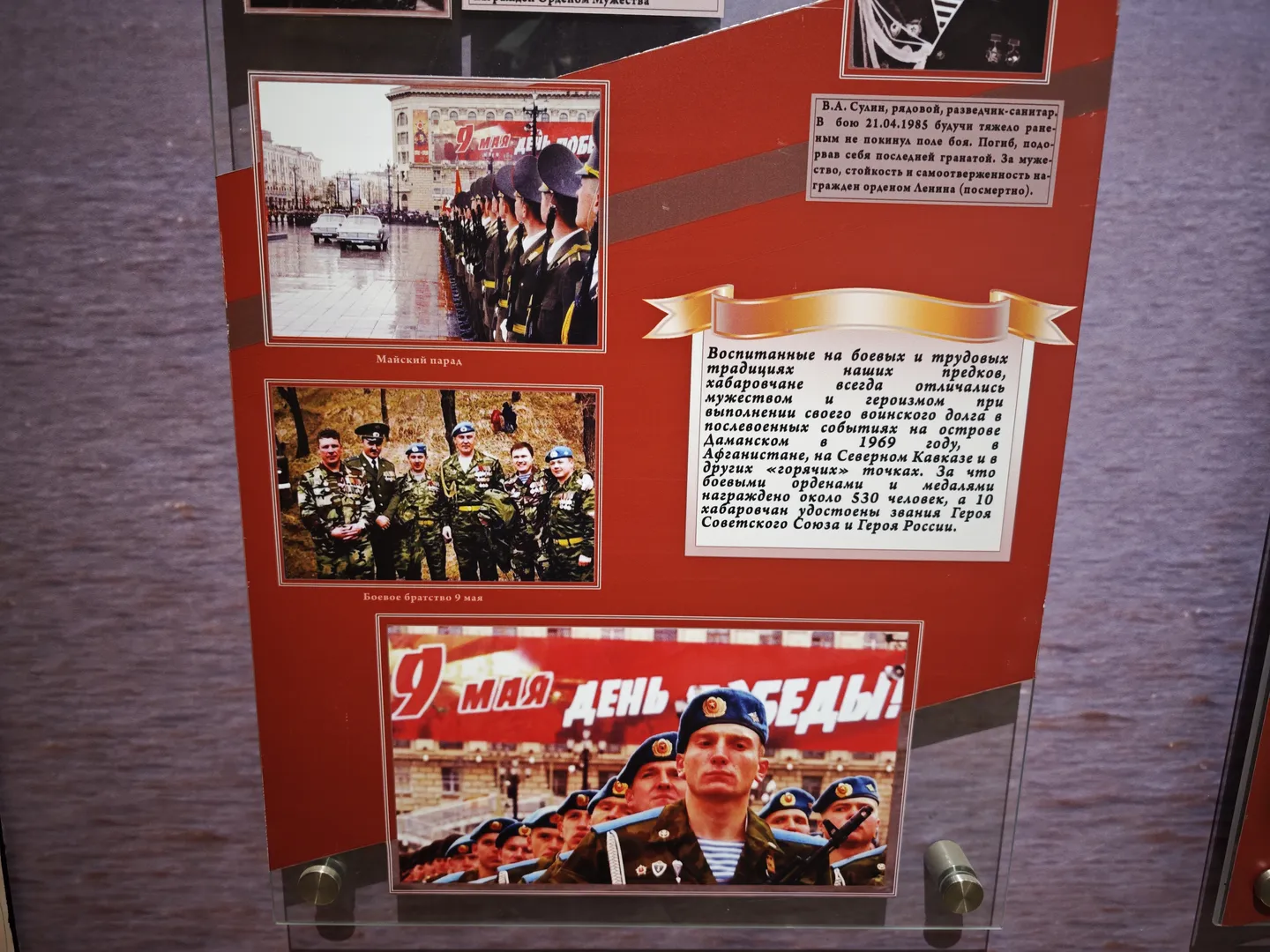展板上有几张军人照片,包括列队行进和集体合影。展板上的文字描述了军人的英勇事迹和荣誉。展板底部有一张“胜利日”庆祝活动的照片。