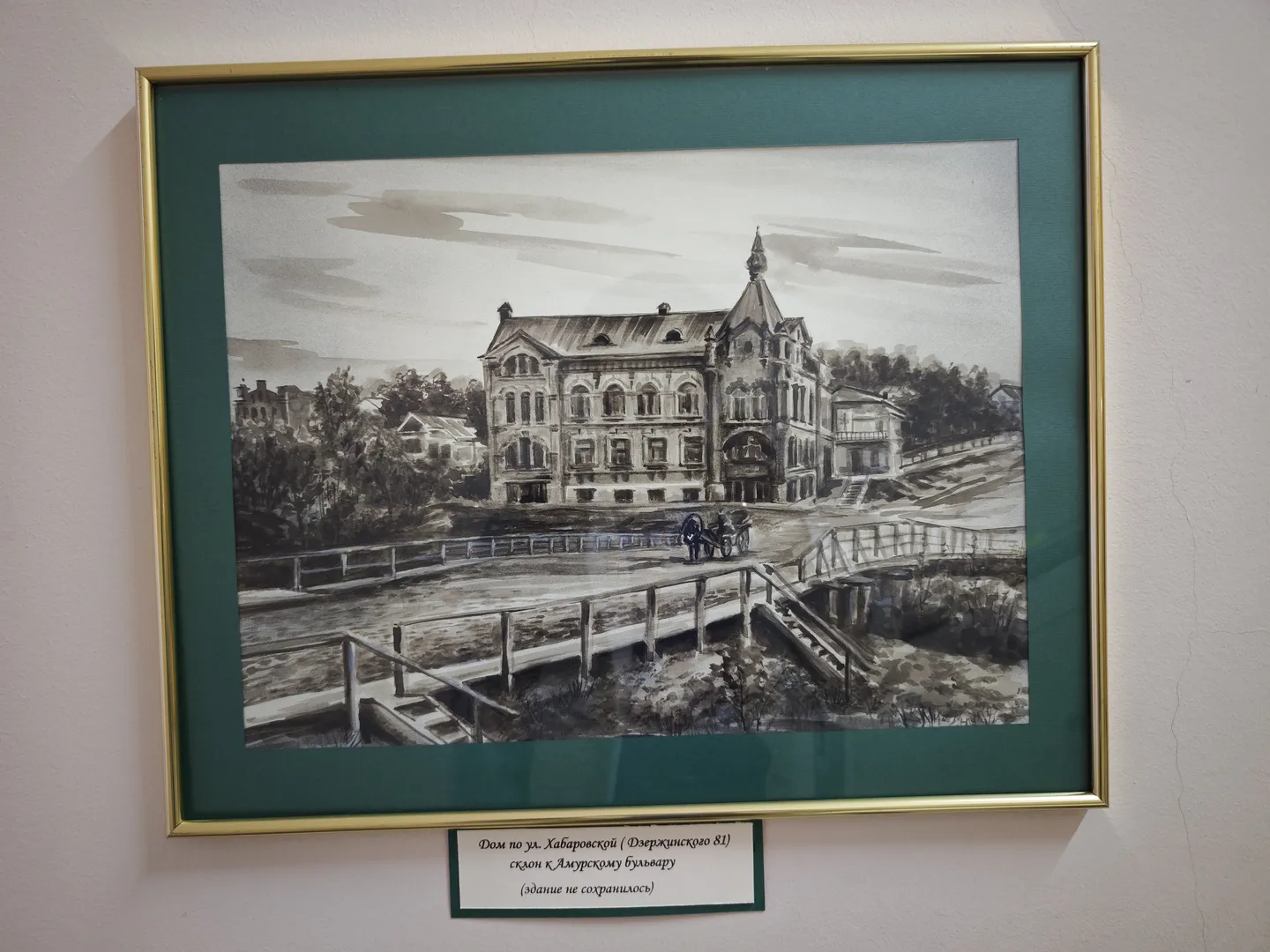另一幅黑白建筑画,描绘了一座带有尖顶和阳台的建筑,前方有一座小桥和两个人推着马车。画作同样装裱在金色边框内,下方有俄文说明。