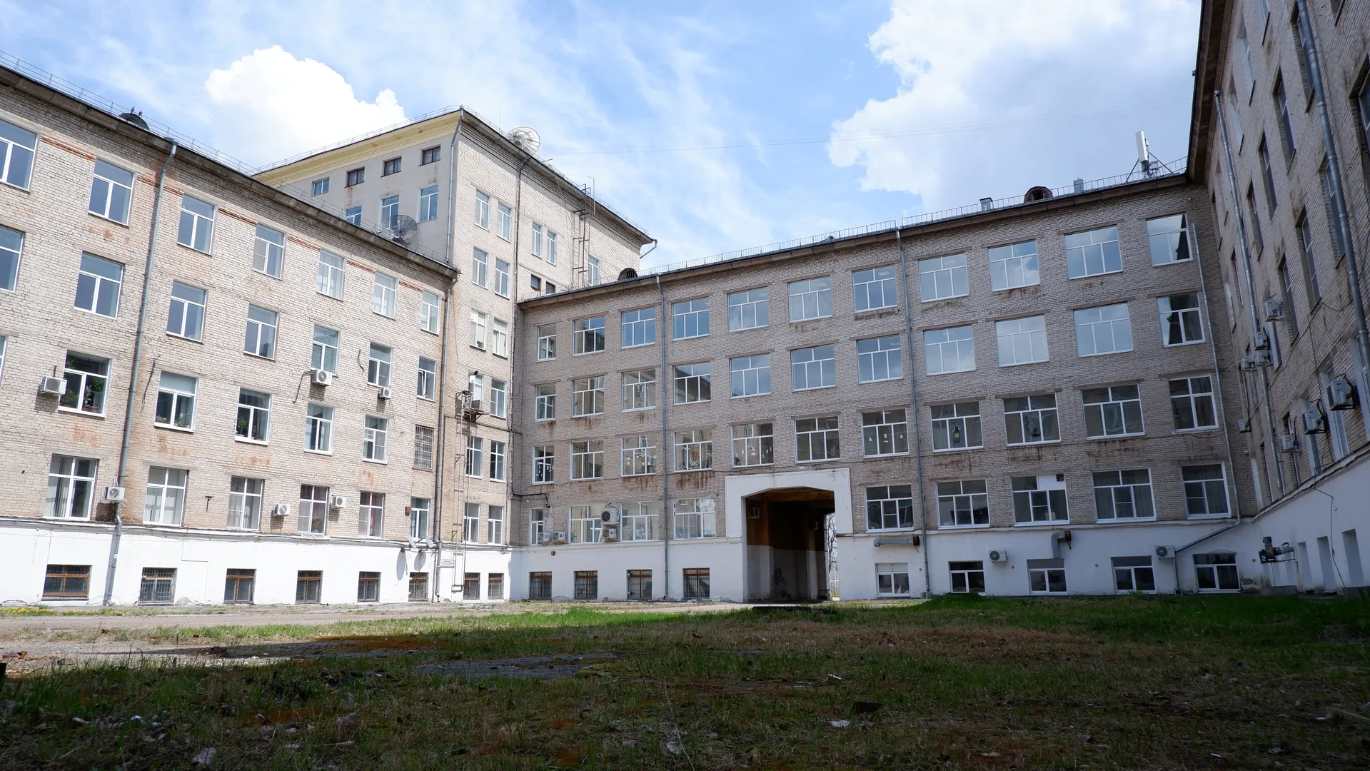 一栋多层建筑,外墙为浅色砖块,窗户排列整齐。建筑前方有一片草地,天空中有几朵白云。建筑物的屋顶上安装了多个卫星天线。