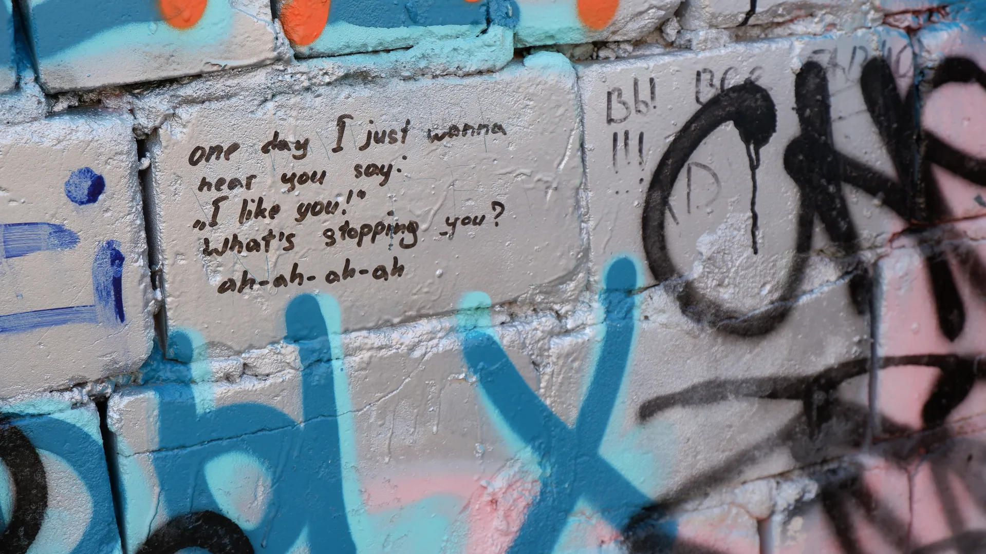 墙上有一段英文涂鸦,内容为“One day I just wanna hear you say: 'I like you!' What's stopping you? ah-ah-ah-ah”。周围有彩色的涂鸦图案。