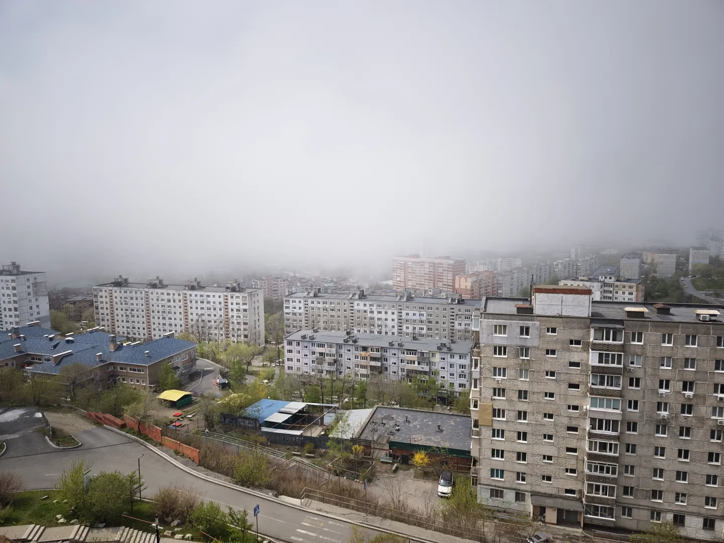 一片住宅区,多层建筑排列整齐,外墙颜色多样。建筑间有道路和绿化带,道路上有车辆行驶。天空布满浓雾,能见度较低。