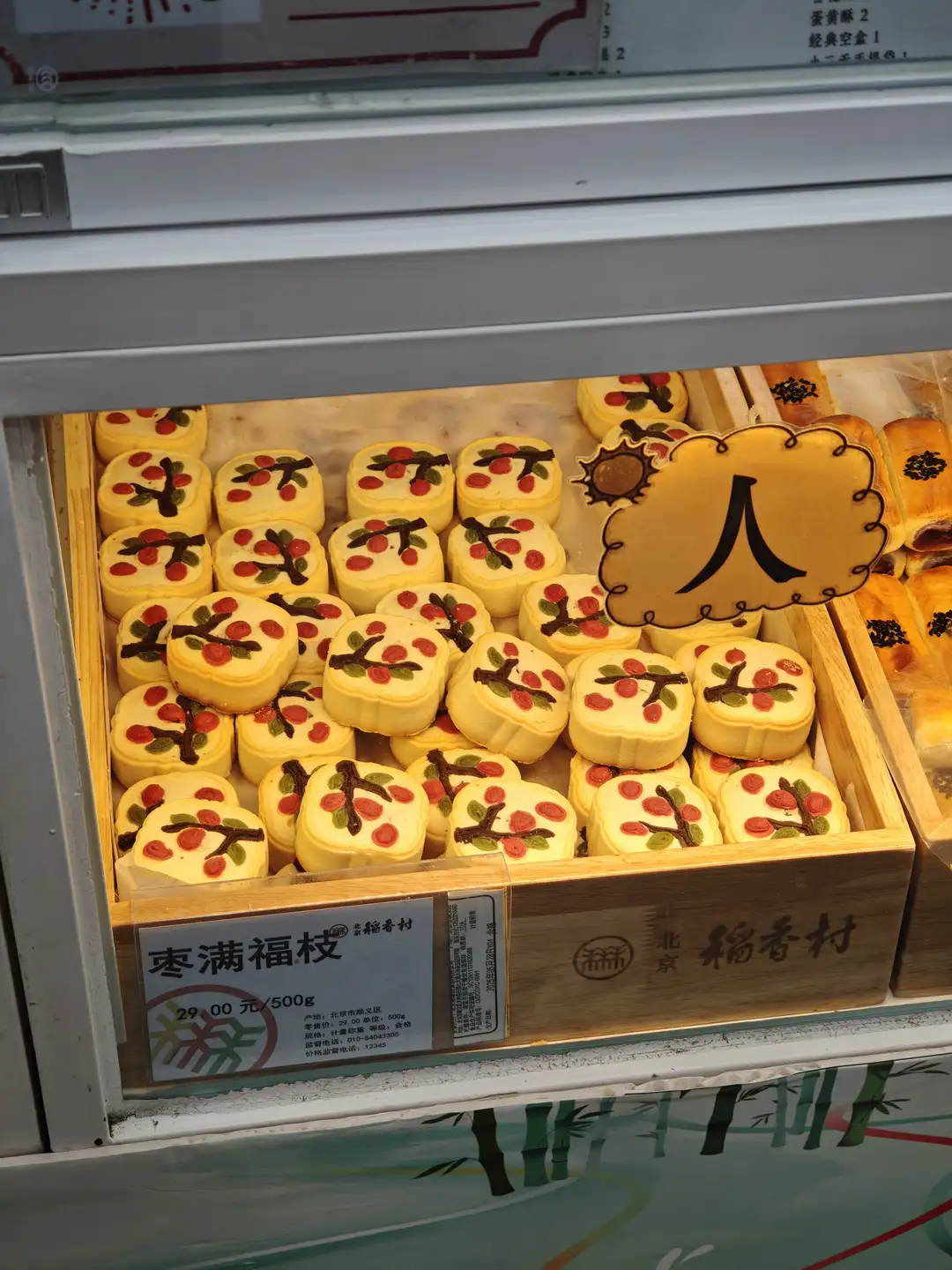 展示柜里陈列着许多黄色糕点,上面装饰有红色果实图案。糕点整齐排列,标签上写着“枣满福枝”。价格为29.00元/500g。