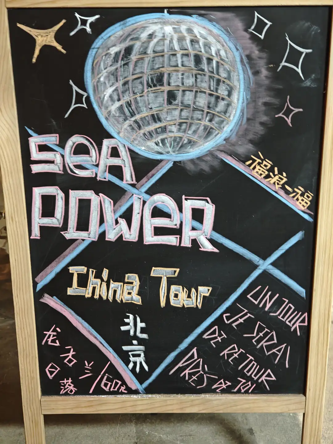 黑板上画着一个迪斯科球,上面写着“SEA POWER China Tour”以及一些中文和法文文字。黑板周围装饰有星星图案,整体设计色彩鲜艳。
