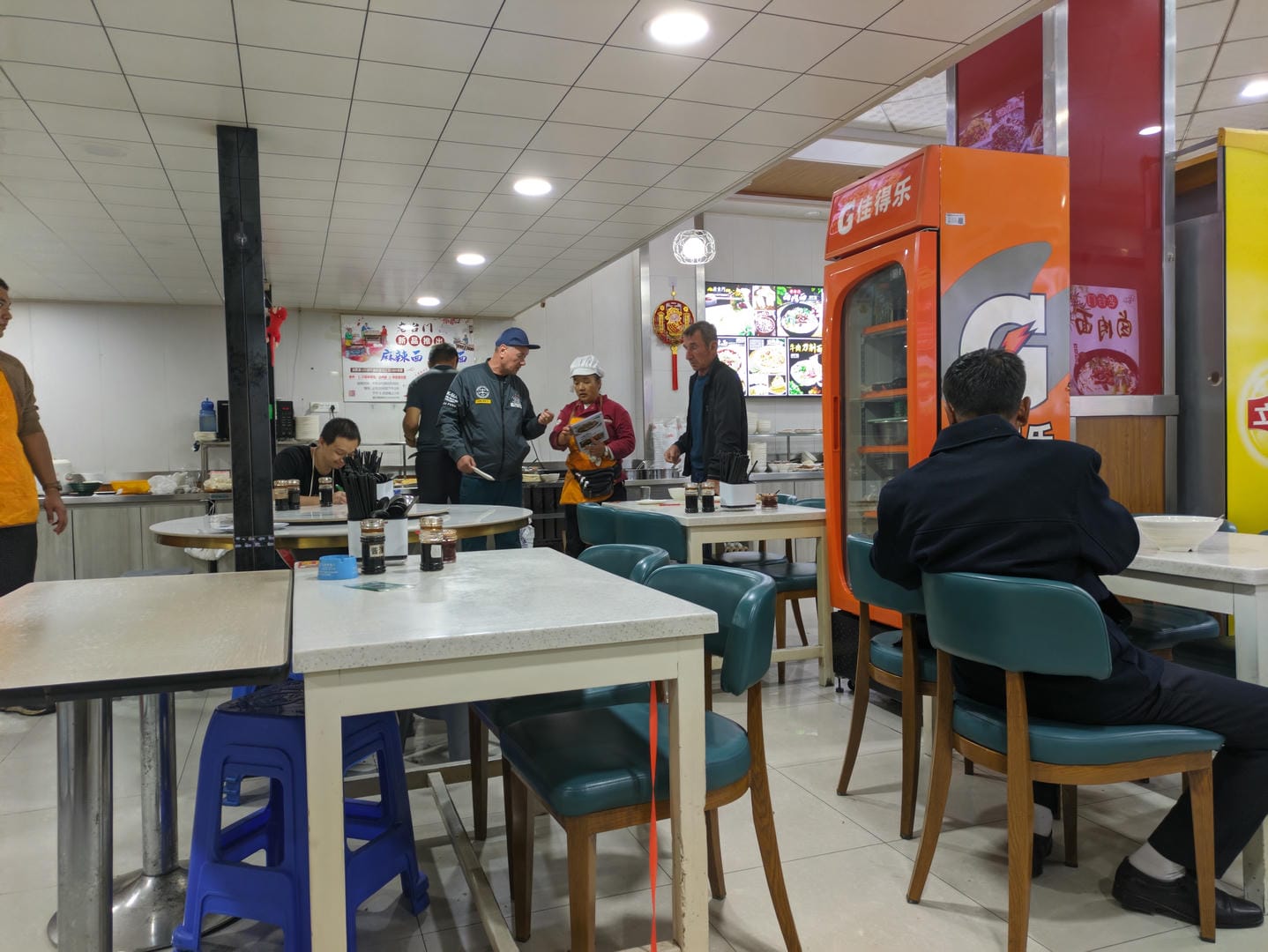 餐厅内,人们坐在桌前用餐,墙上挂着菜单。