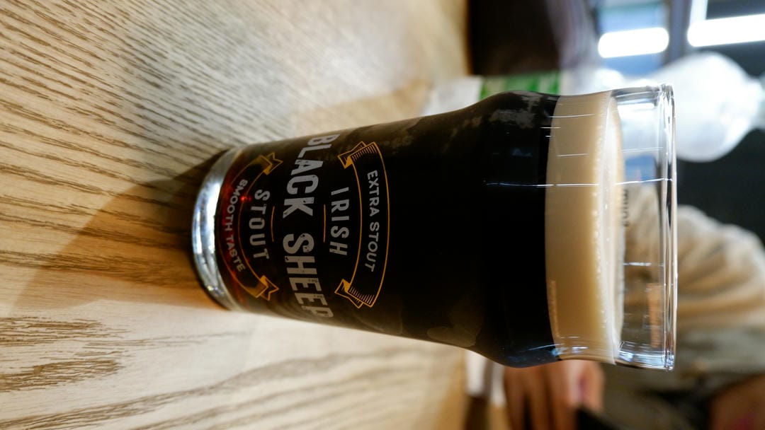一杯名为“Irish Black Sheep Stout”的啤酒放在木桌上。