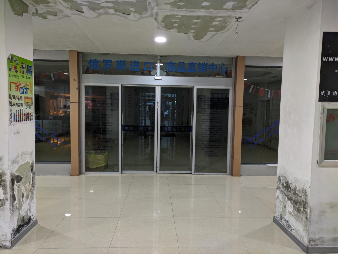 室内场景,玻璃门上贴有蓝色中文标识,墙壁有剥落痕迹。