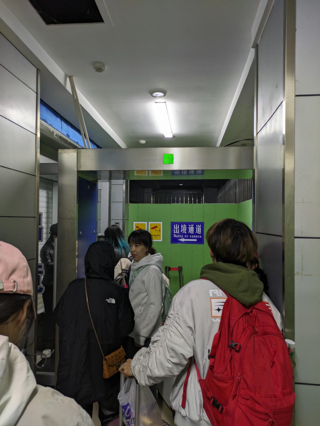 几个人在通道内等待,通道尽头有一个绿色出口标志,指示“出境通道”。