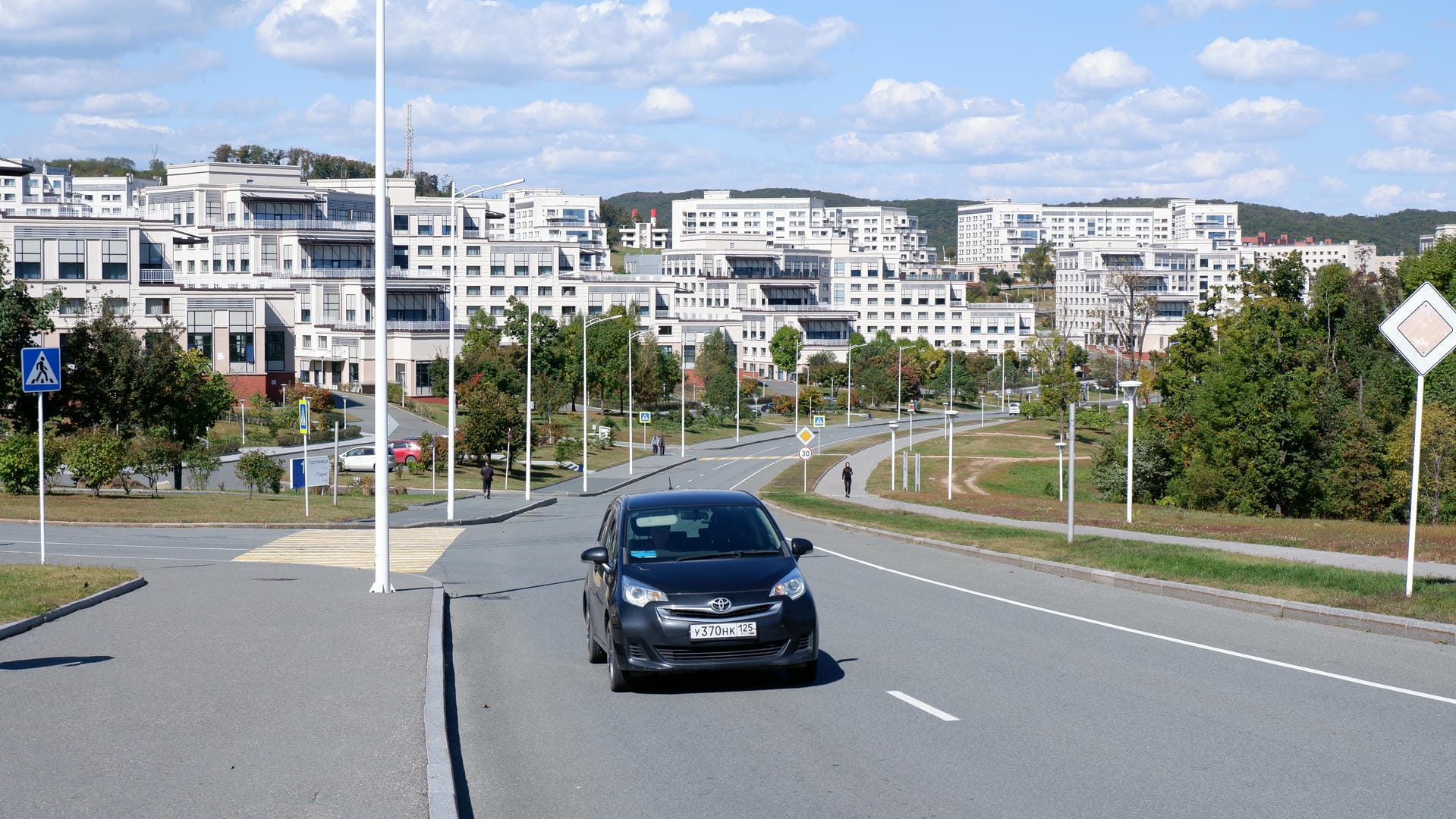 一辆黑色汽车行驶在道路上，背景是许多白色建筑。