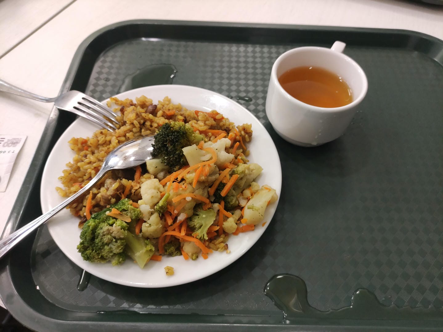 托盘上有一盘炒饭、蔬菜和一杯茶,旁边放着餐具。