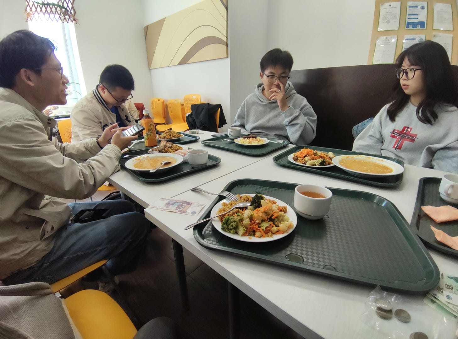 四个人围坐在餐桌旁,面前有食物和饮料,其中一人在看手机。