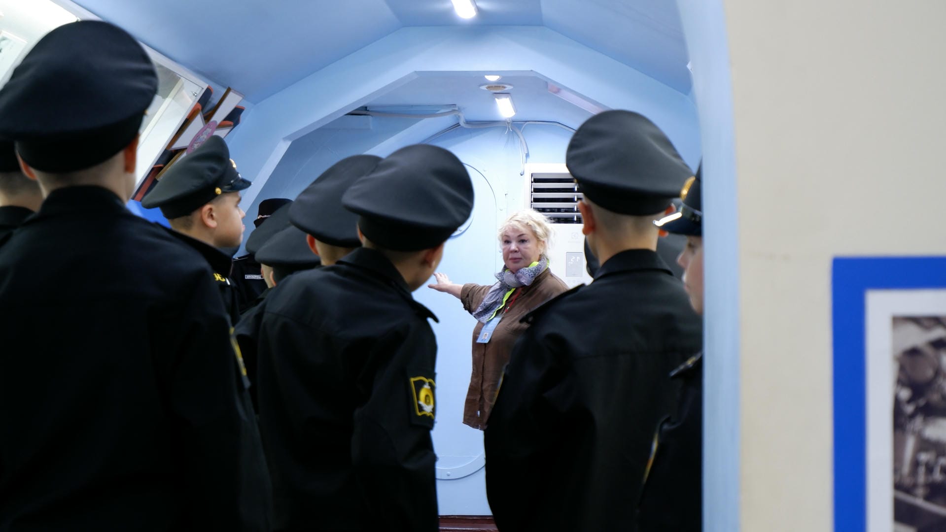 一群穿着制服的学生在听一位女士讲解。