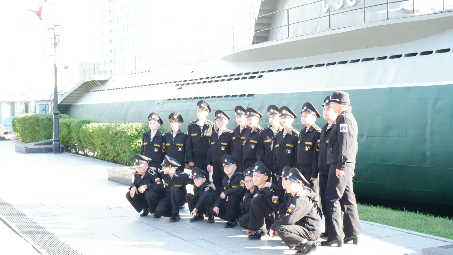 一群穿着海军制服的孩子站在一艘潜艇前，背景是晴朗的天空。