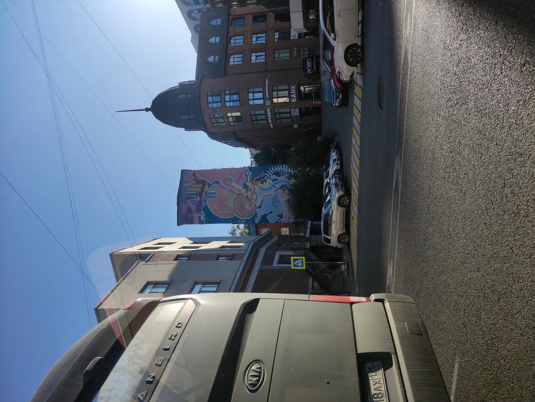 街道上有建筑物和车辆,左侧有一辆灰色的汽车,远处有彩色壁画。