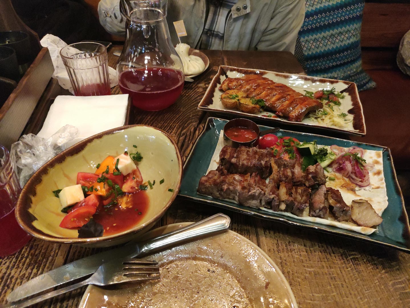 餐桌上摆放着烤肉串、排骨、沙拉和一杯红色饮料,餐具整齐放置。