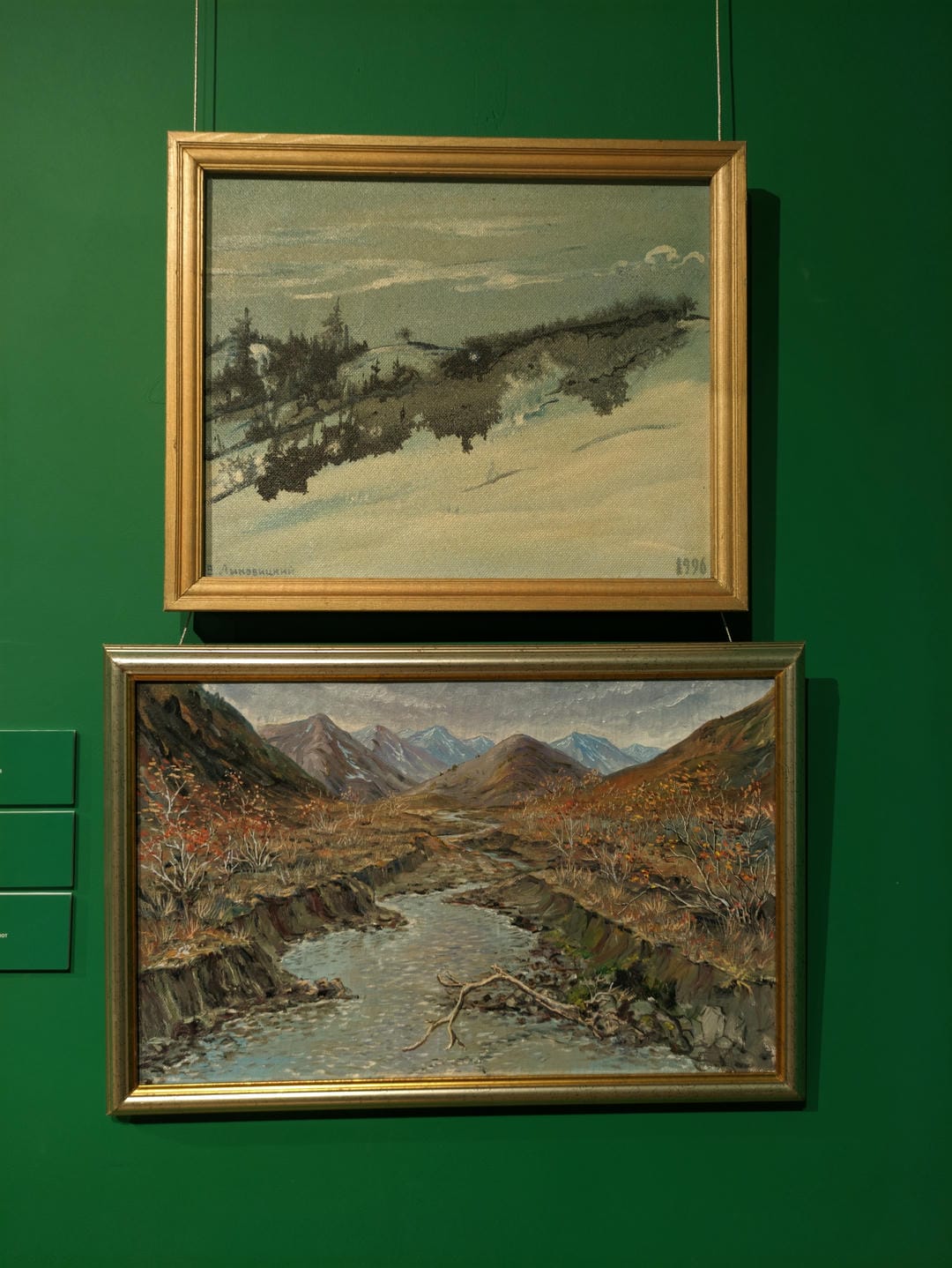 两幅画作挂在绿色的墙上,上方的画描绘了雪景中的树木,下方的画展示了山间小溪和秋天的景色。