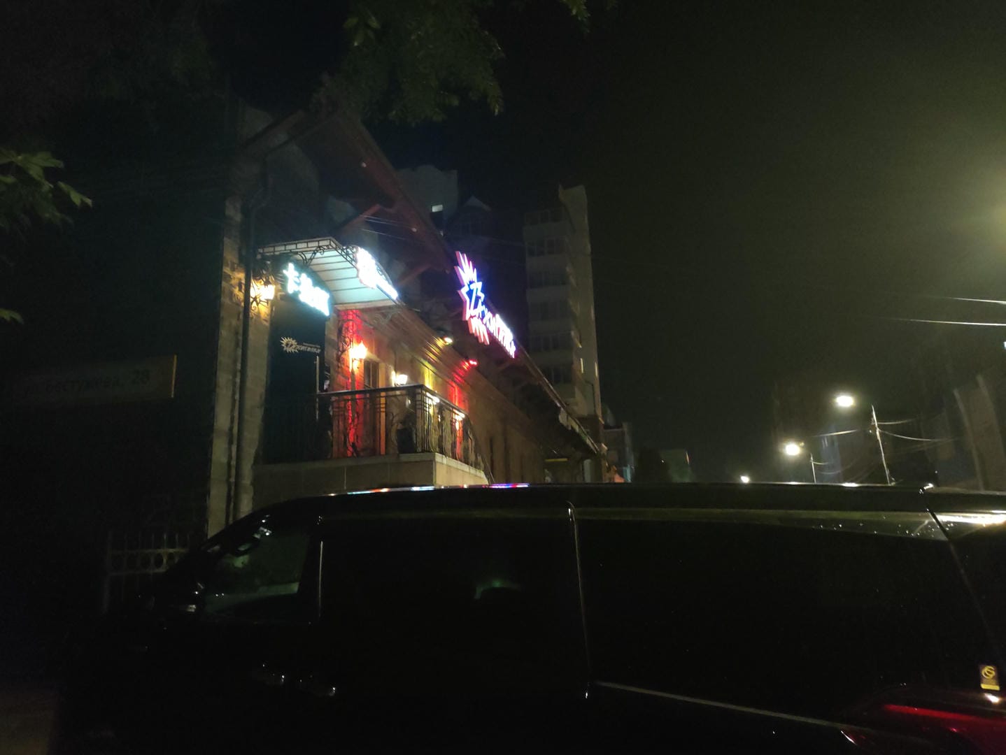 夜晚的街道上有霓虹灯招牌的建筑物和一辆黑色汽车。