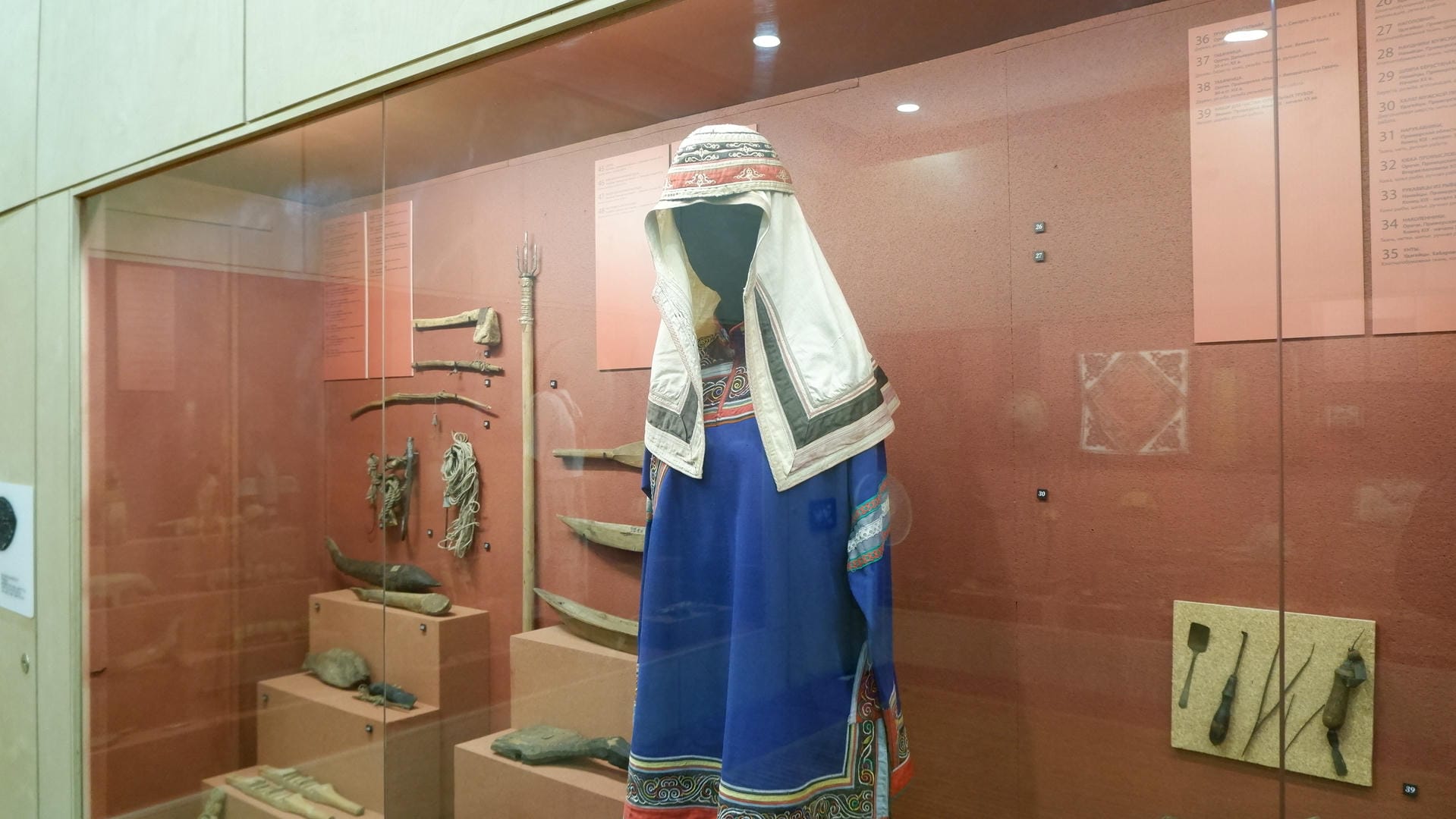 一件蓝色的传统服饰挂在展示柜中央，周围是其他文物。