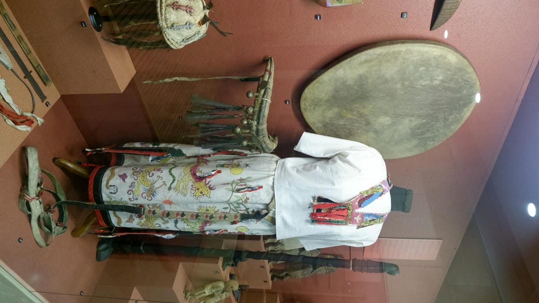 一套传统服饰展示在一个木制支架上，旁边有一个圆形鼓和其他物品。