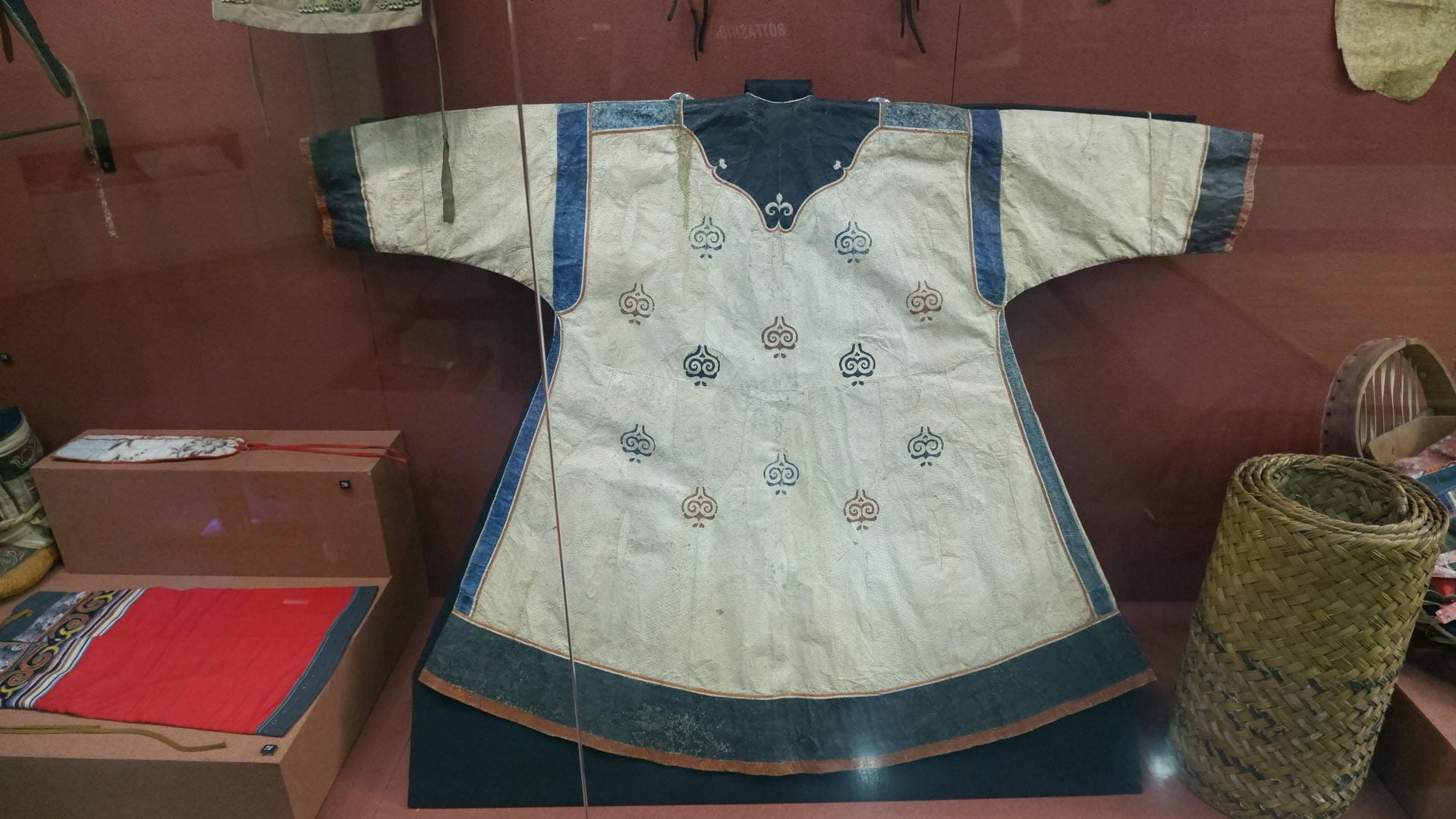 一件白色长袍平铺在展台上，上面有蓝色花纹装饰。