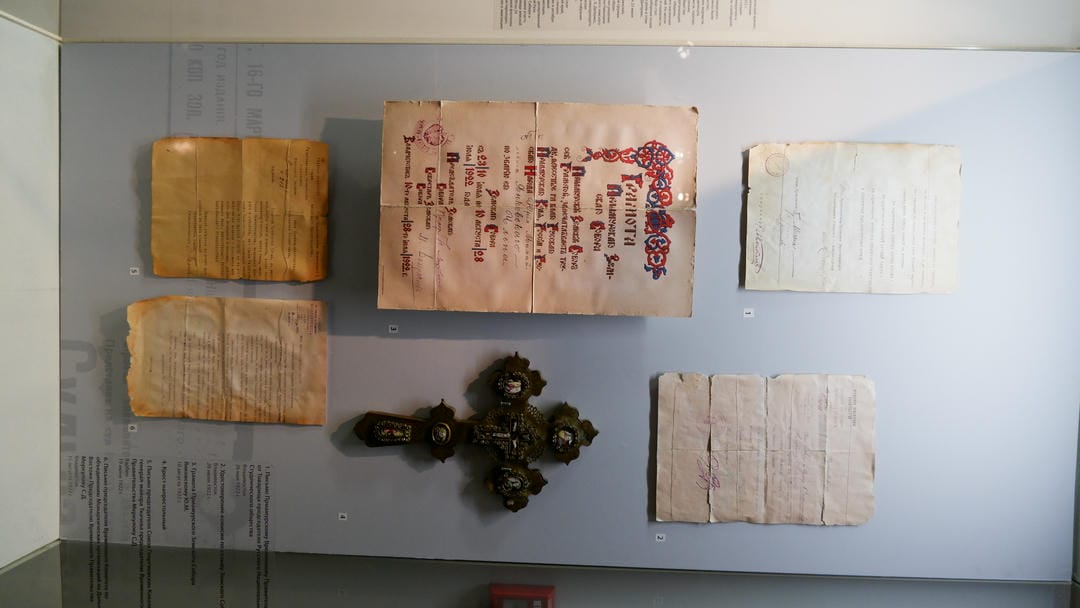多份旧文件和一个十字架展示在玻璃柜中。