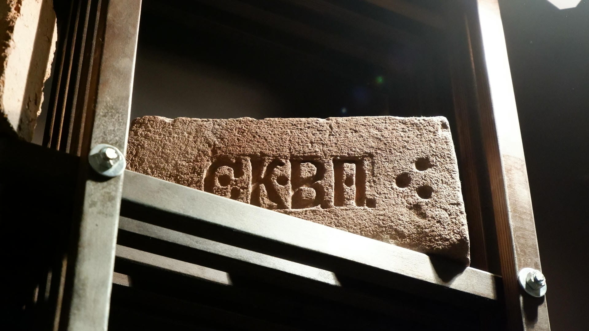 一块刻有“G.K.B.P.”字样的石板，被金属框架固定在墙上。