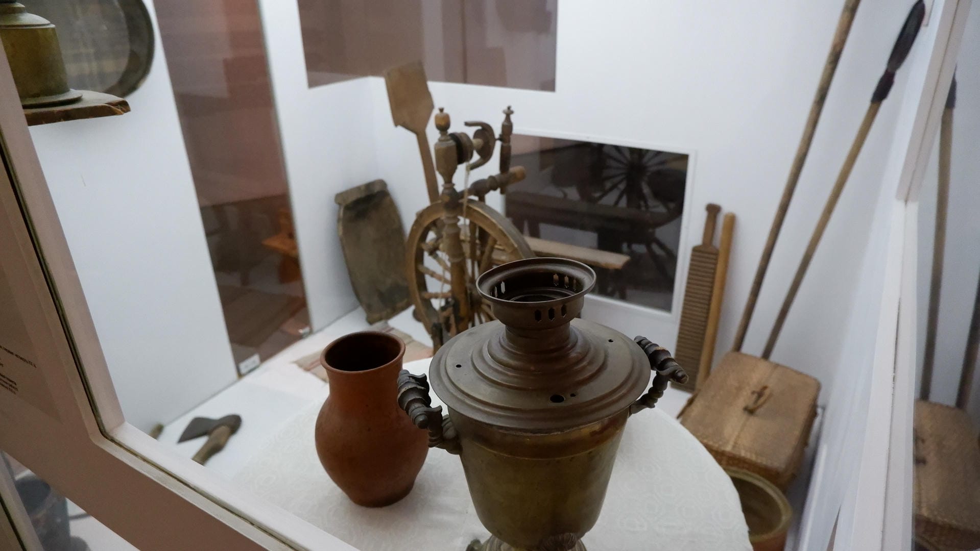 一个陶瓷壶和一个金属容器展示在一个玻璃柜中，背景中可以看到一些木制工具。