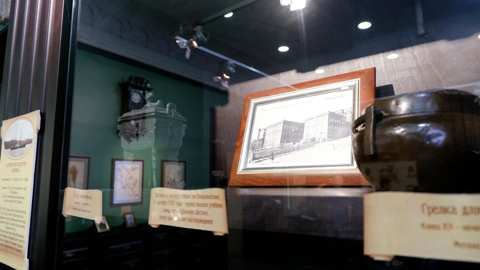 一个玻璃展示柜内，展示了一幅建筑物的画作、一个绿色雕塑和其他物品。