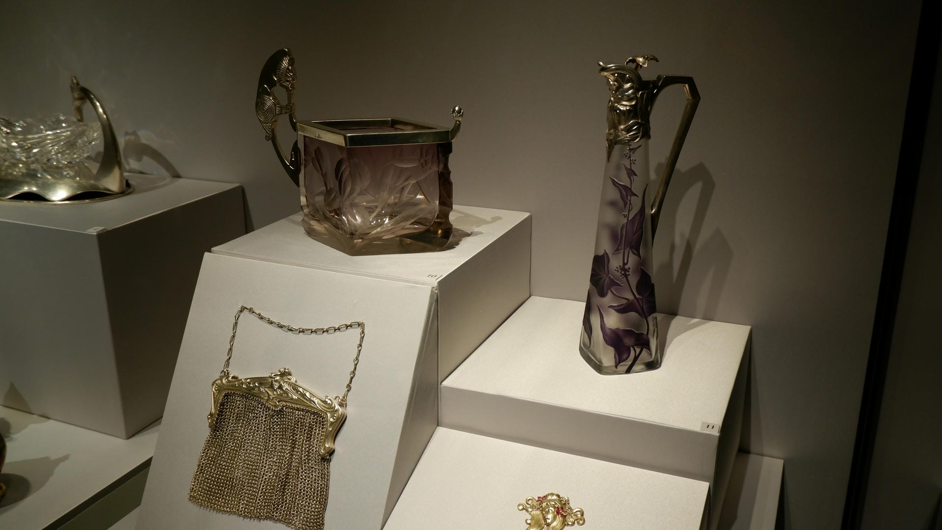 展示柜中有两个高脚杯和一个手提包，杯子上有花卉图案，手提包由金属链条制成。