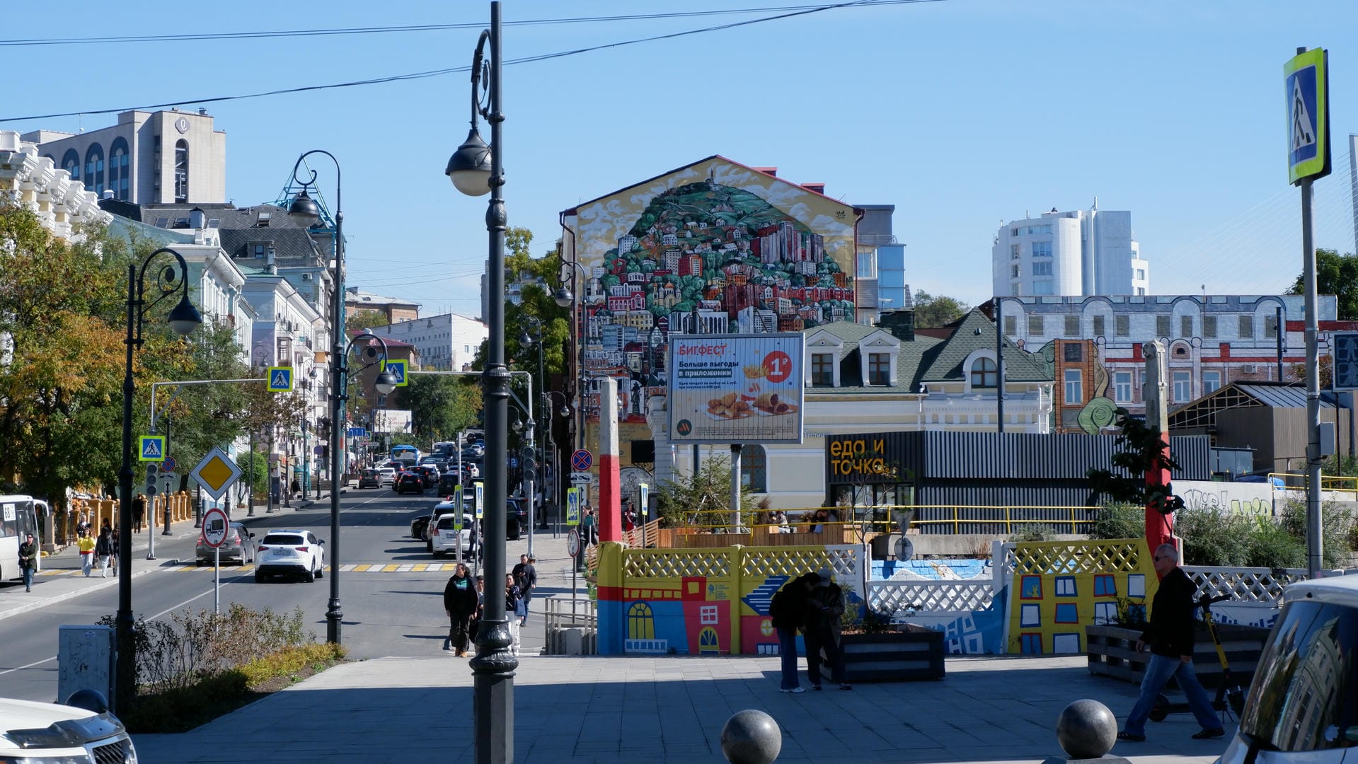 街道两旁是建筑物，远处有一幅大型壁画，描绘了城市风光。