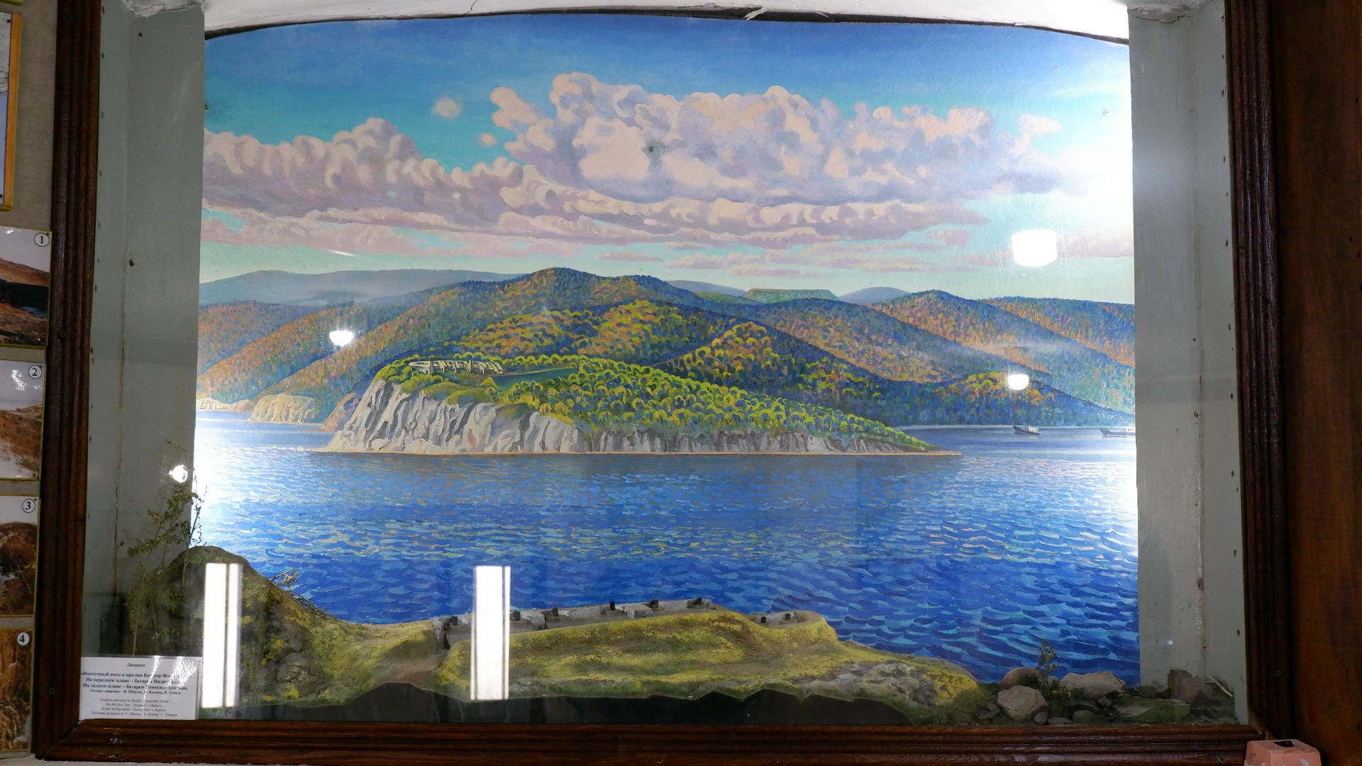 一幅描绘湖泊和山脉的画作，天空中有云朵，前景有模型地形。