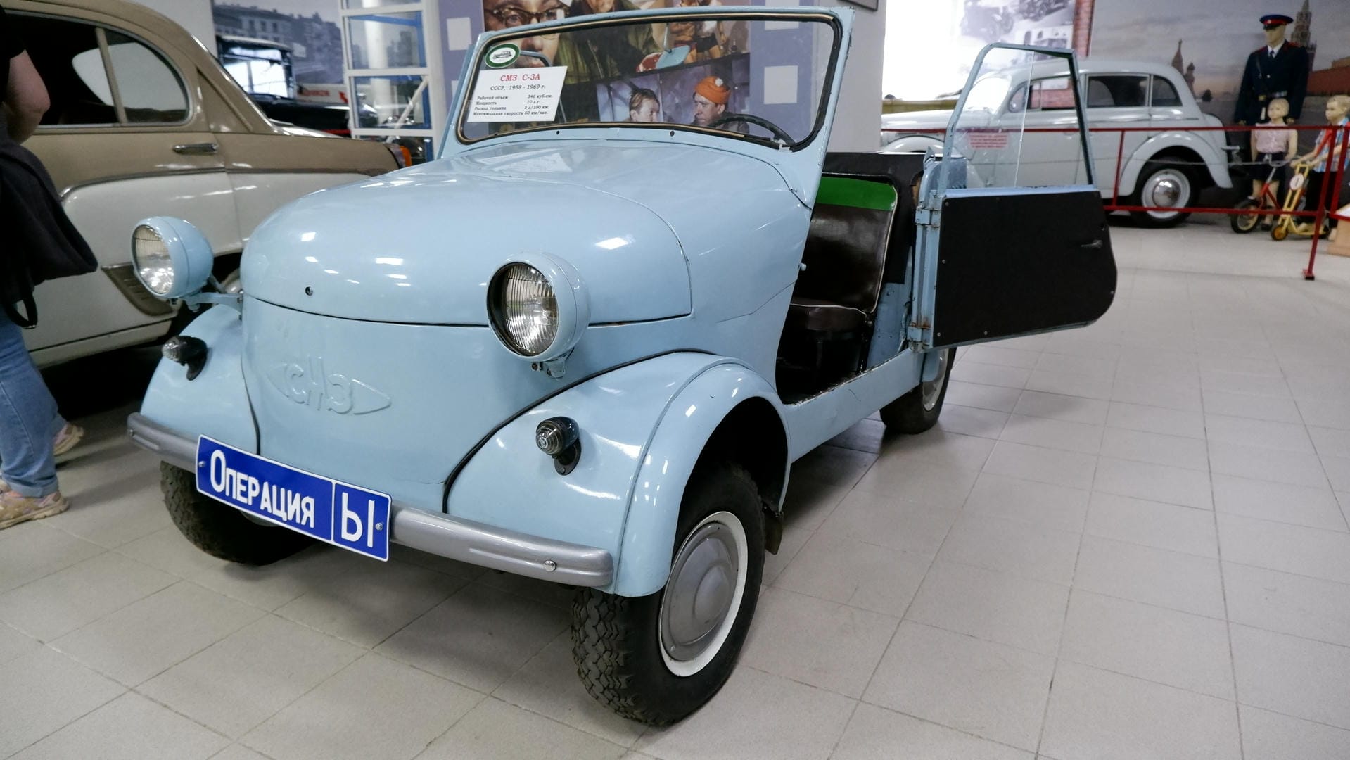 一辆浅蓝色的小型复古汽车，车门打开，车牌上写着“ОПЕРАЦИЯ ы”。