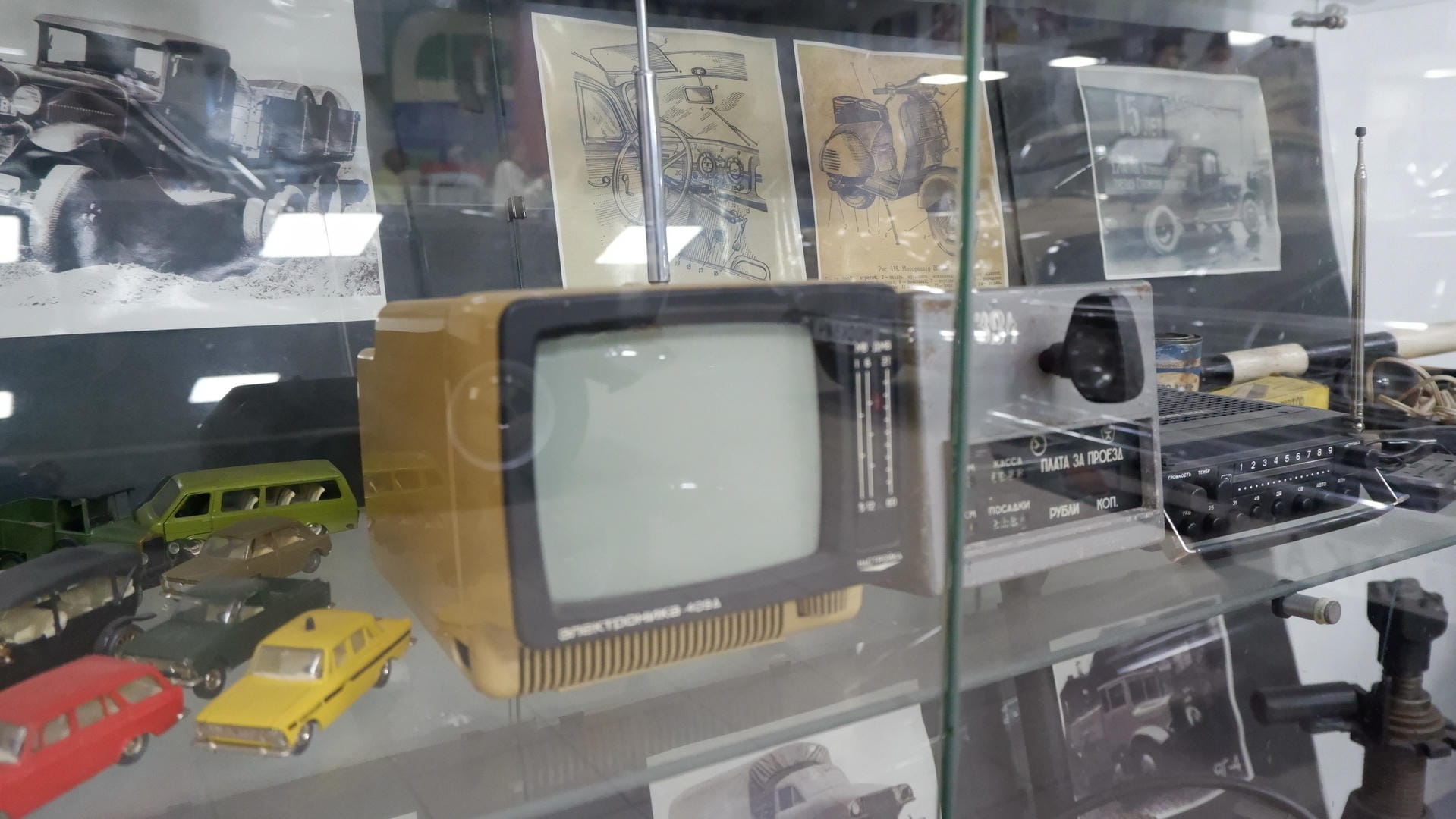 一个展示柜内摆放着一台老式电视机、收音机和其他物品，背景有汽车图纸。