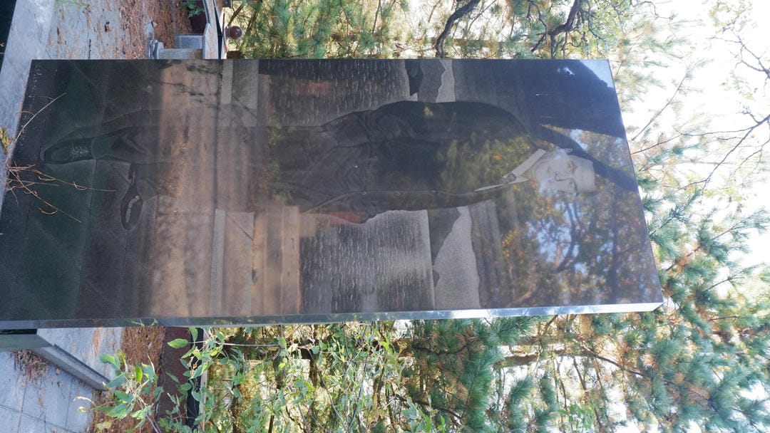 墓碑上刻有男性肖像，背景是树木和天空。