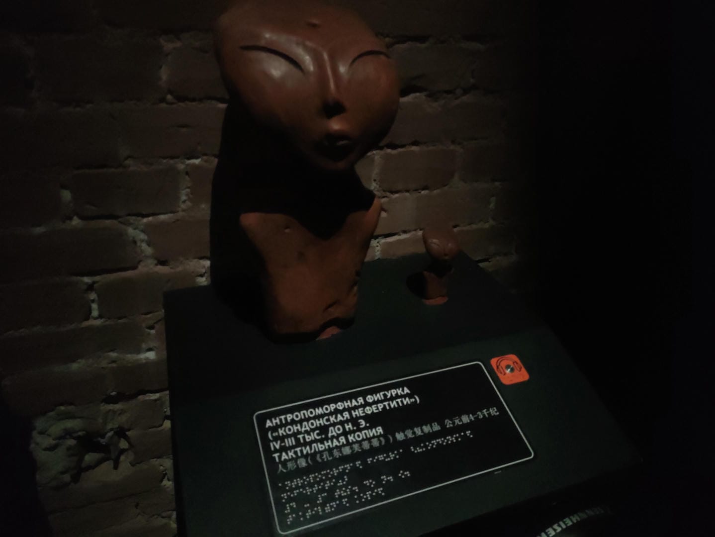 一个棕色的人形雕塑,没有手臂,面部表情平静,背景是砖墙。