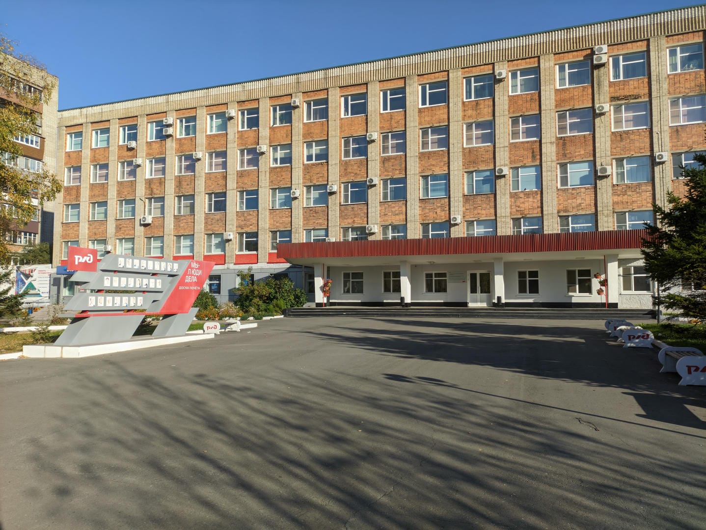 一栋多层建筑前有一个红色雕塑,建筑外墙上挂着空调室外机。