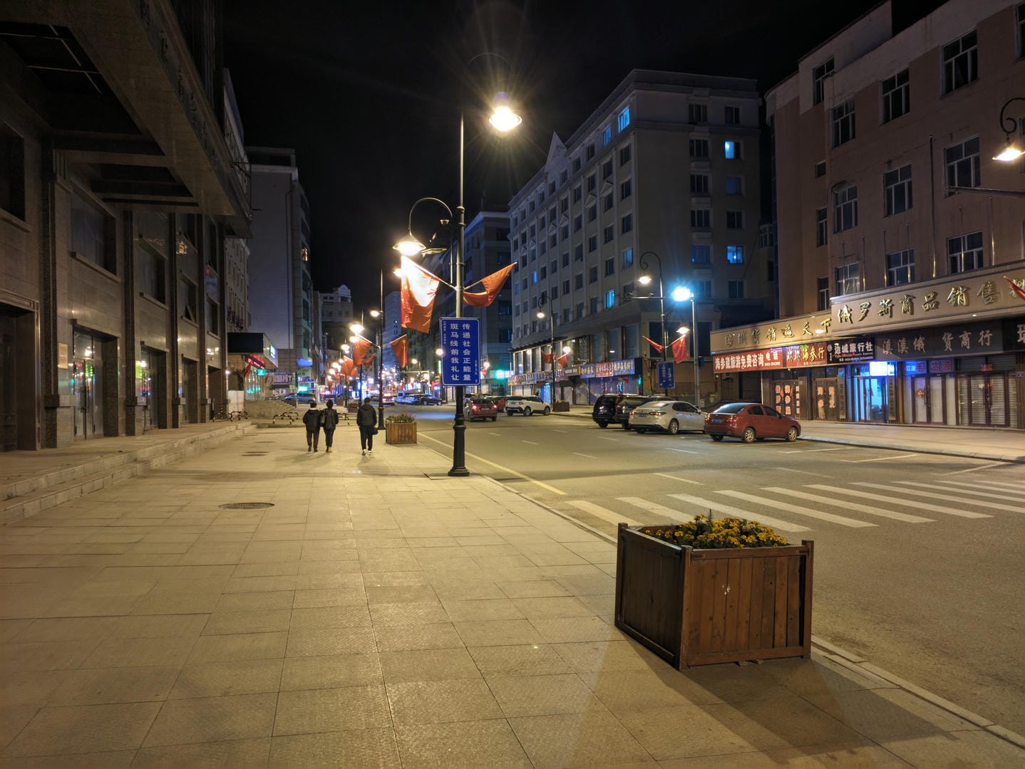 夜晚的城市街道,路灯亮着,两个人在人行道上行走。