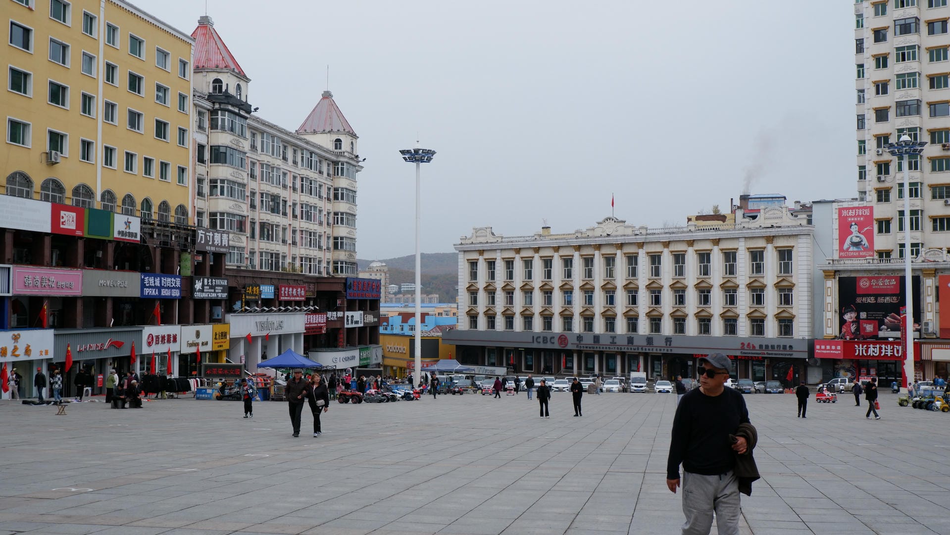 一个广场，周围有多栋建筑物，包括一座白色和黄色相间的建筑，广场上有几个人在行走。