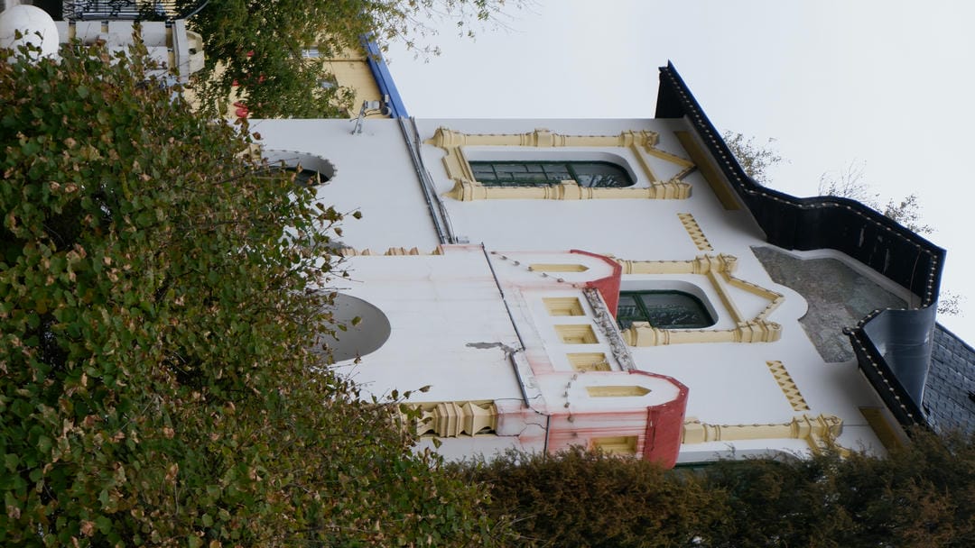 一栋白色建筑的一部分，建筑风格独特，窗户装饰精美，前景有一些绿色植物。