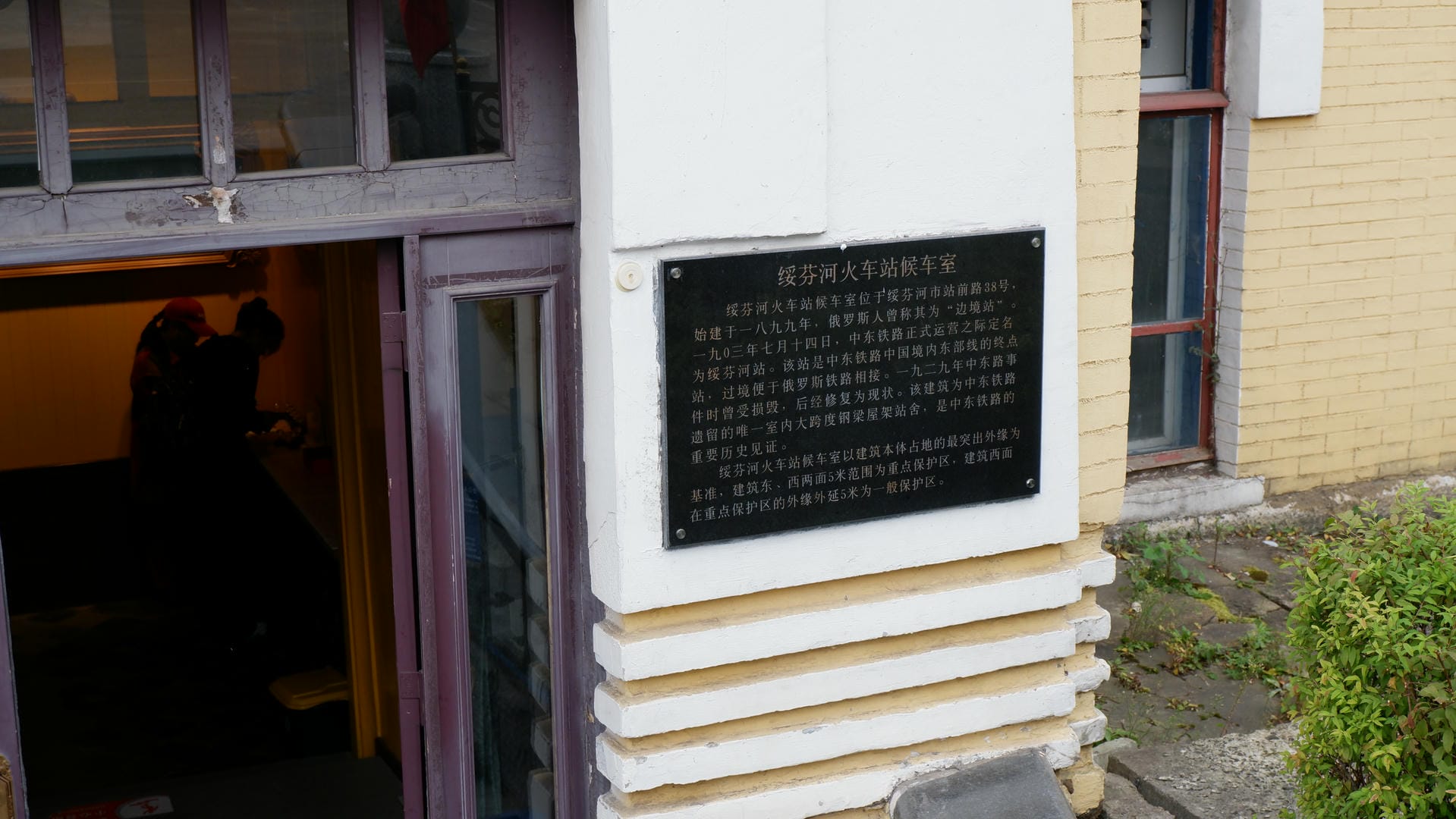 一扇门旁边有一块黑色金属牌匾，上面用中文书写着关于绥芬河火车站候车室的历史信息。