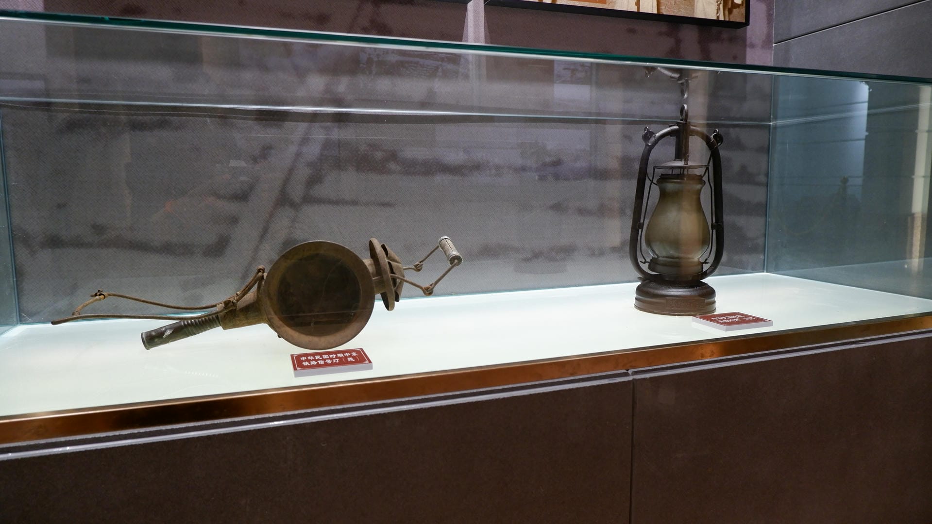 玻璃展柜里展示着一个铜制喇叭和一盏煤油灯。