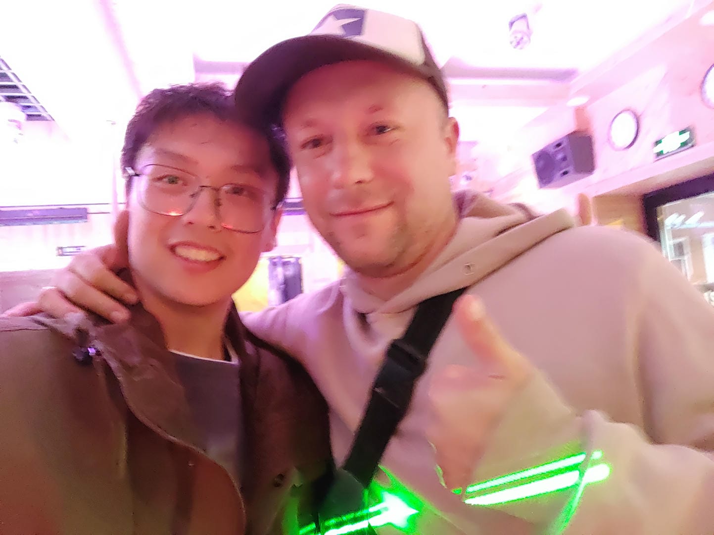 两个人在室内自拍,背景有粉色灯光和装饰。