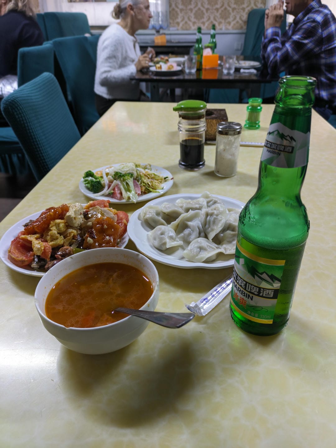 餐桌上摆放着饺子、炒菜、汤和一瓶啤酒。